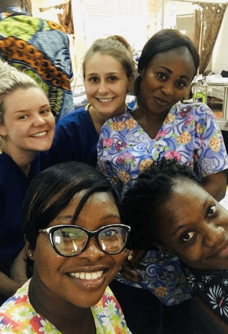 Courtney and Emily with local healthcare workers in patterned scrubs taking a group selfie.