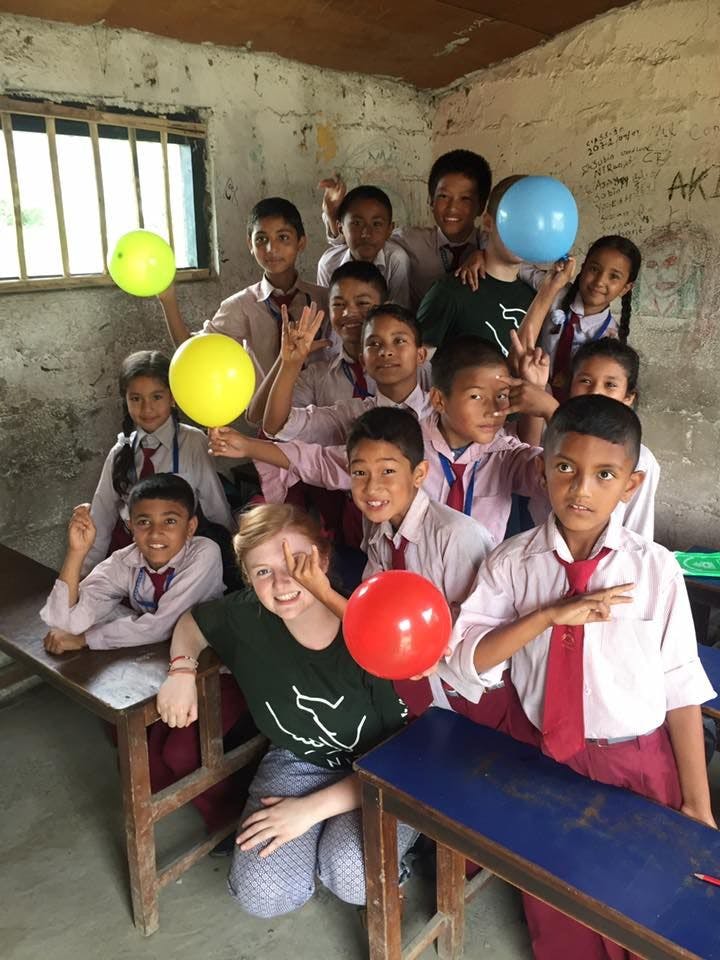 Group of students in uniforms posing with balloons inside a classroom, along with Hollie.