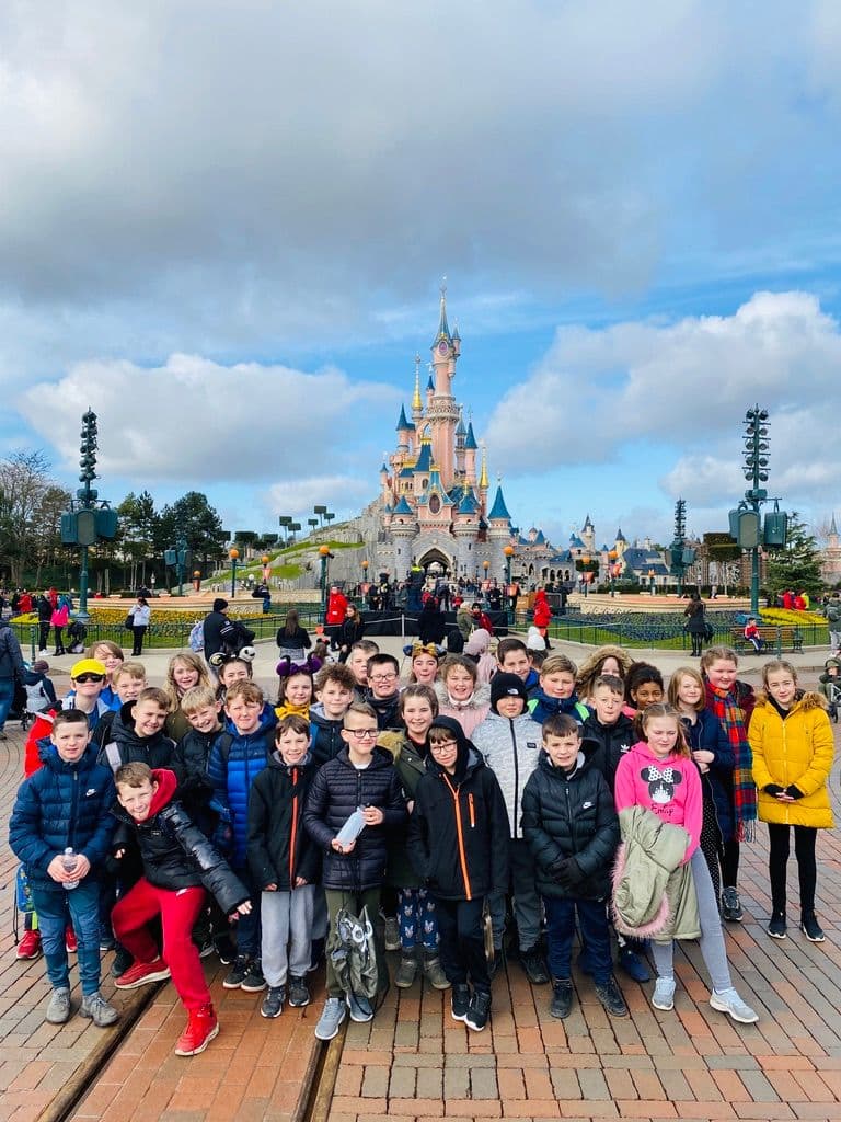 Children posing for a photo in front of the sleeping beauty castle at Disneyland Paris.