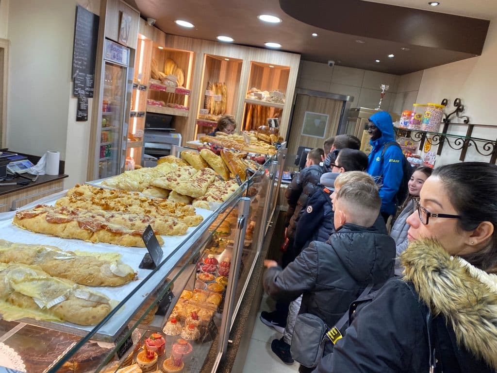 Children waiting in line at a bakery with an array of baked goods on display.